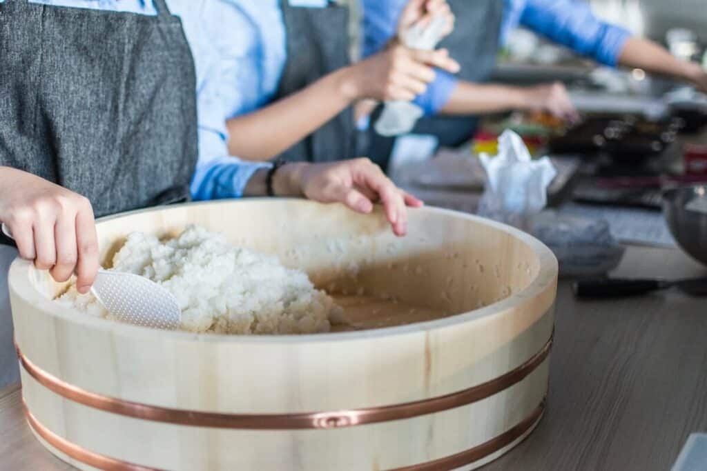 A chef scooping out Japanese rice from a wooden bowl