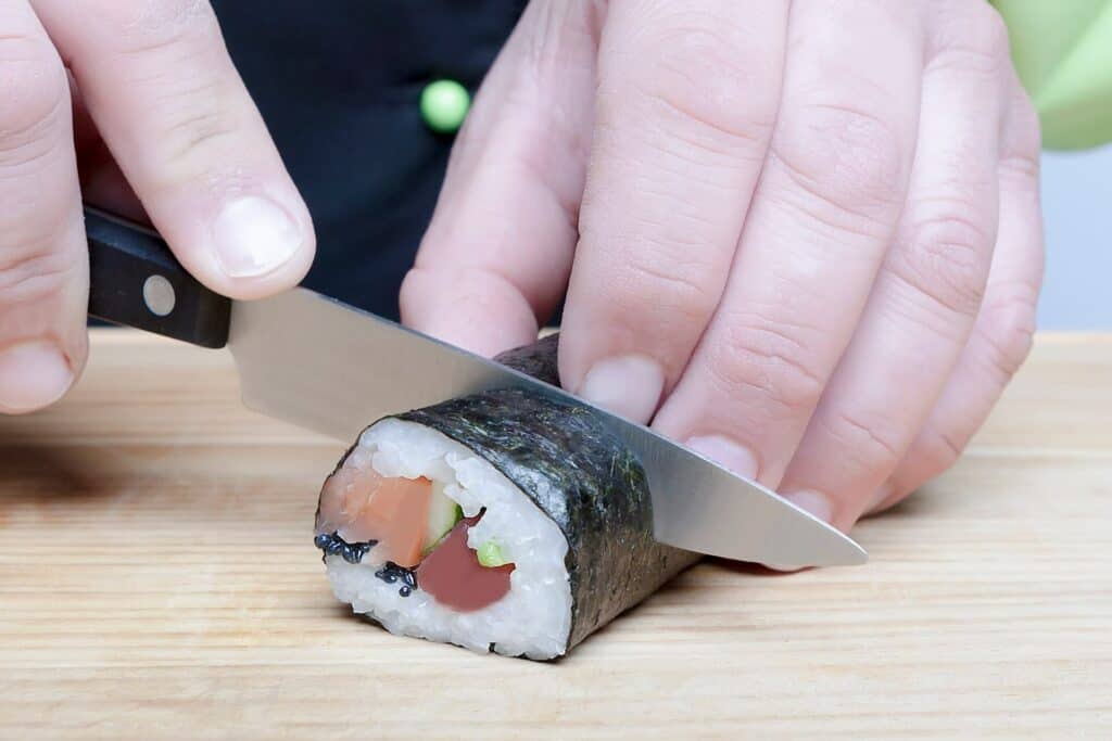 A person cutting a sushi roll
