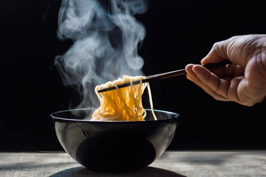 Person picking up ramen noodles from a bowl with chopsticks