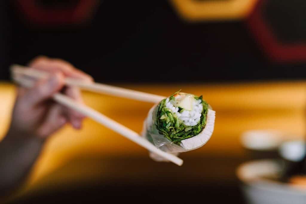 A person holding a sushi roll with chopsticks