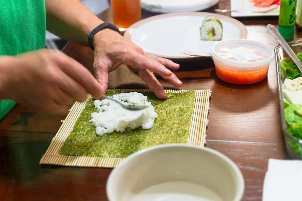 A person off-screen making sushi rolls