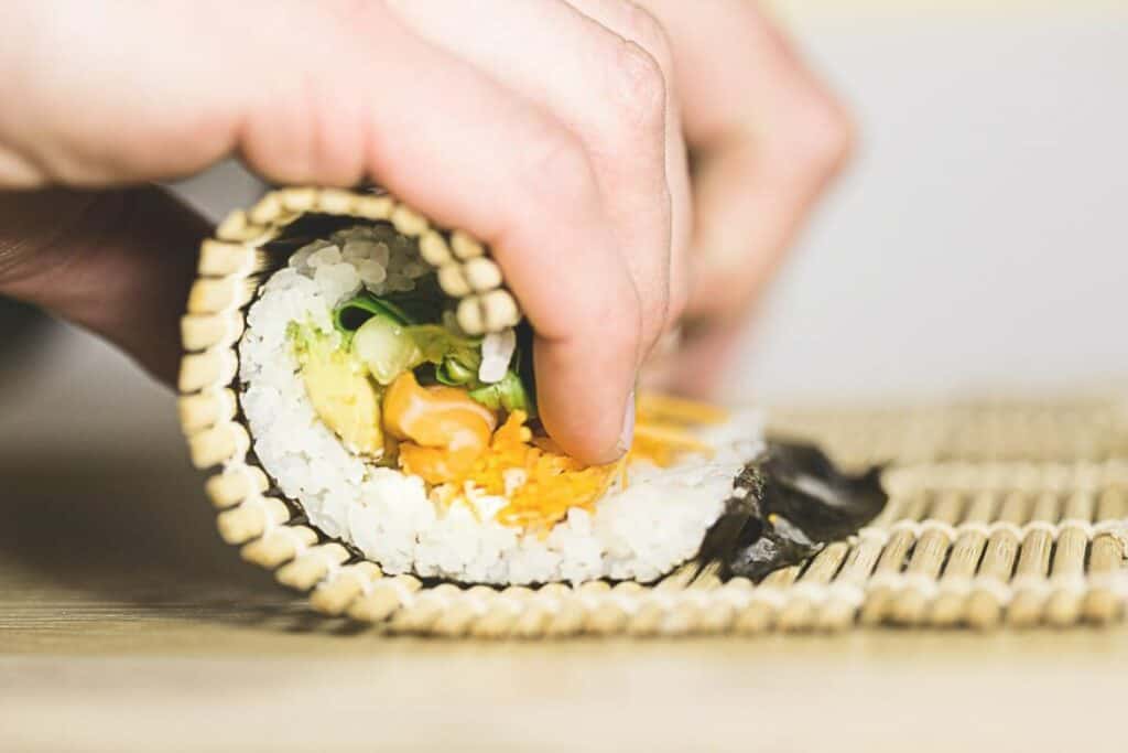 A person off-screen rolling sushi with a bamboo mat