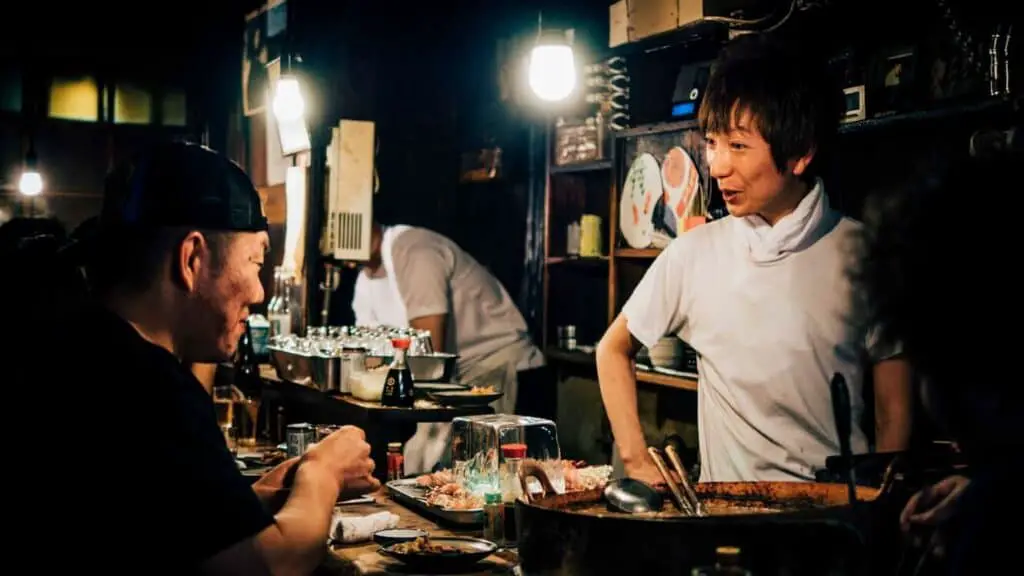 A sushi chef talking with a customer who's eating