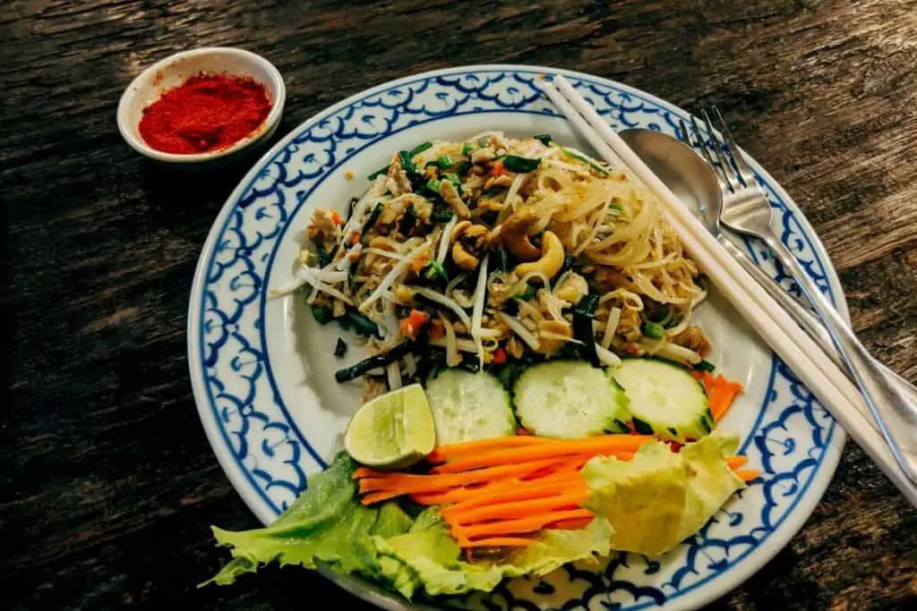 A plate of pad thai with a salad and spice