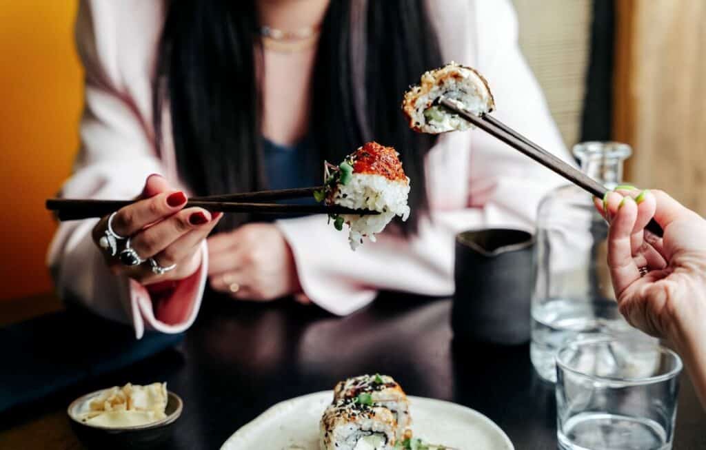 Two women eating sushi with chopsticks in a restaurant