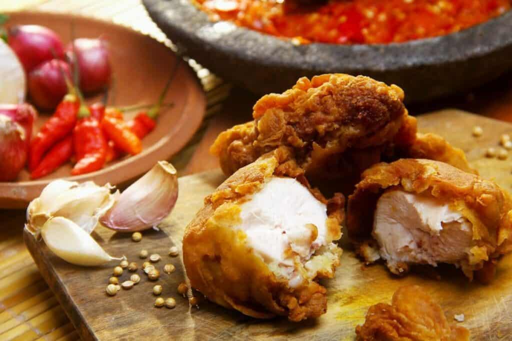 A few pieces of fried chicken laid out on a cutting board with some garlic