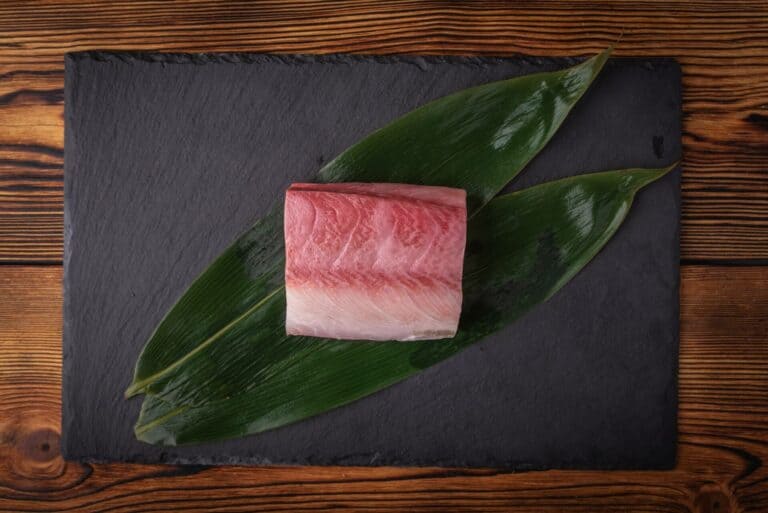 A block of hamachi and two leaves on a black serving board
