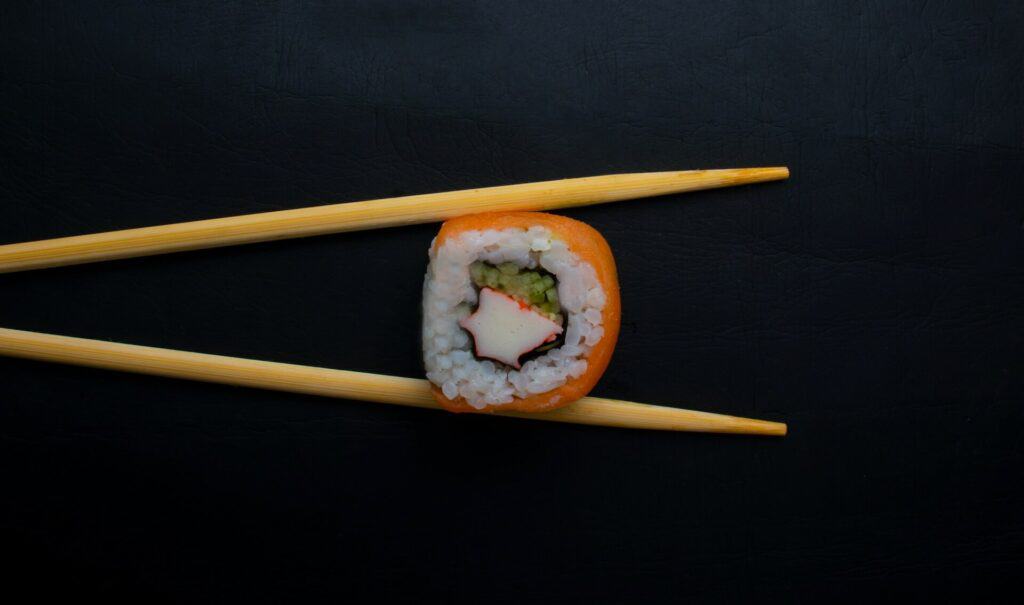 A sushi roll between two wooden chopsticks