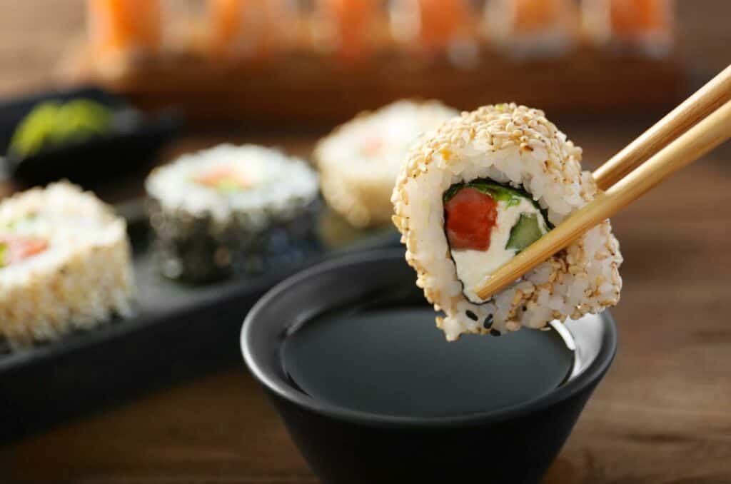 Bowl of soy sauce and five sashimi rolls, one held by chopsticks