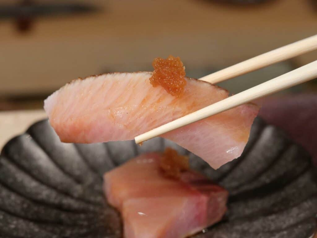 A slice of sashimi held by food sticks