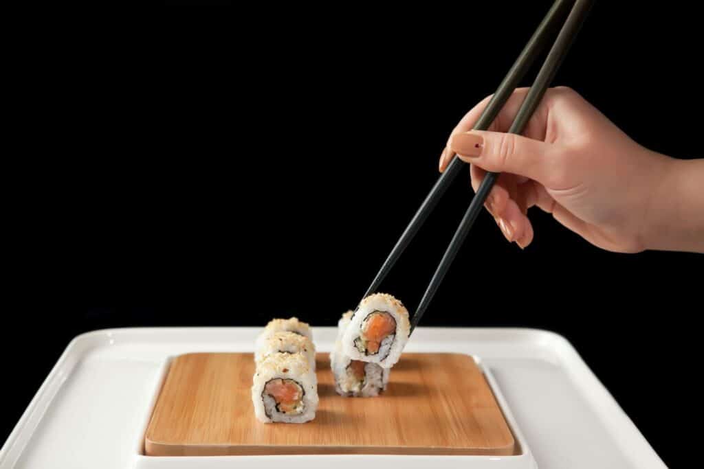 A person off-screen taking one California roll of the wooden plate