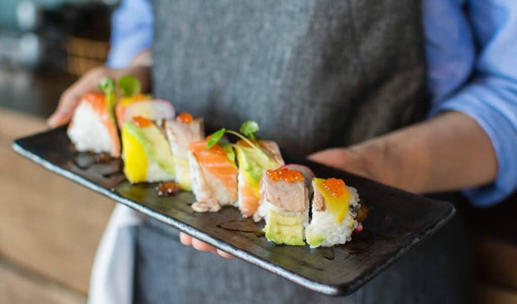A person holding several different sushi rolls on a plate