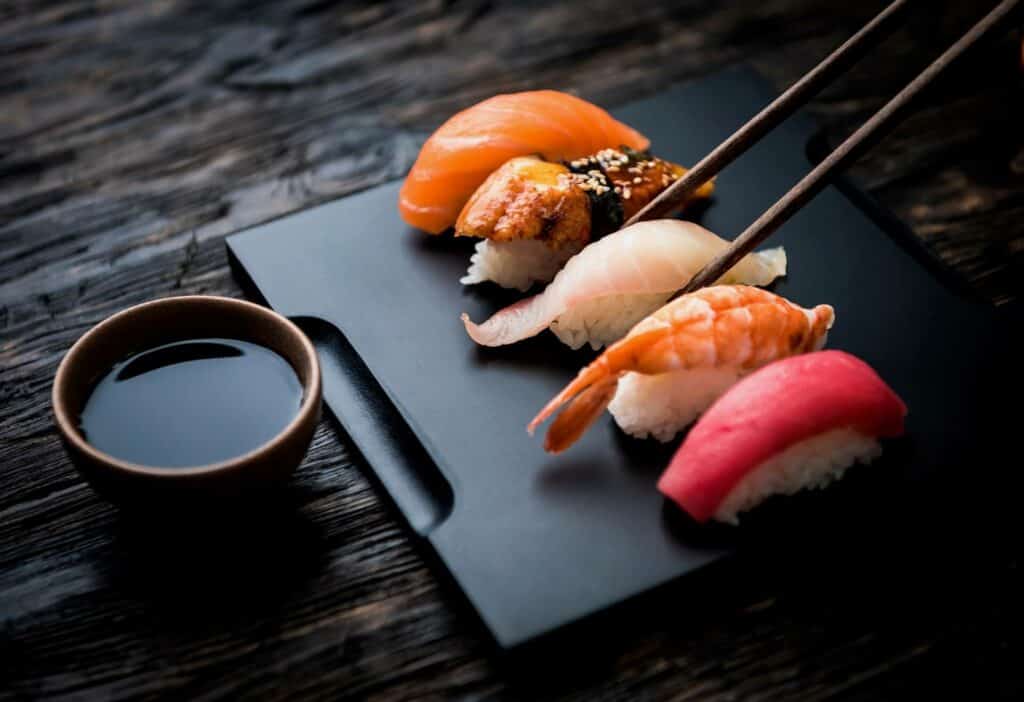 Sushi roll held by chopsticks above a tiny bowl with soy sauce
