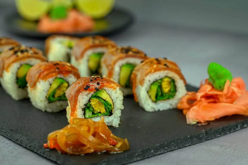 A few different sushi rolls placed on a plate with some pickled ginger