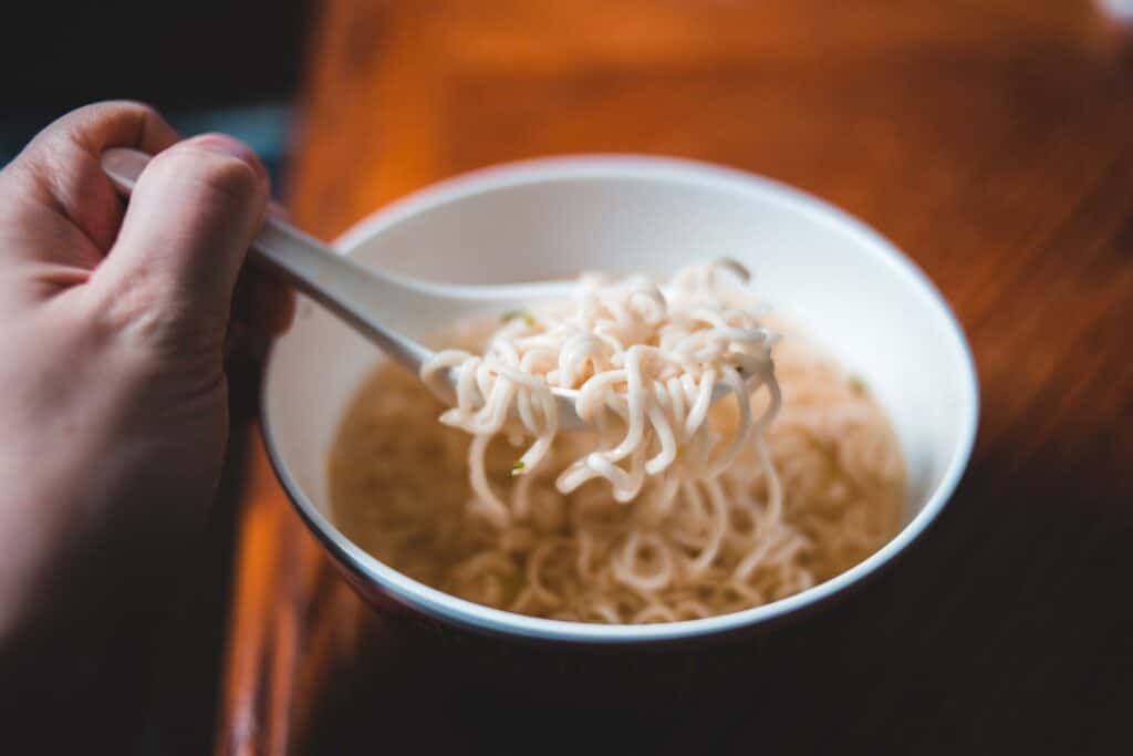 A picture of a plain, cooked noodle dish and a person scooping them up