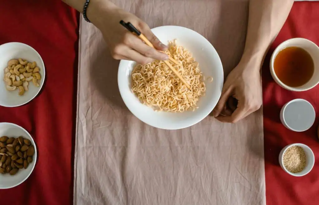 A woman off-screen preparing to season her noodle container