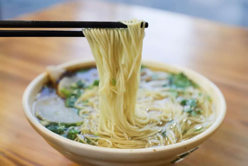 Chopsticks holding noodles over a bowl of soup