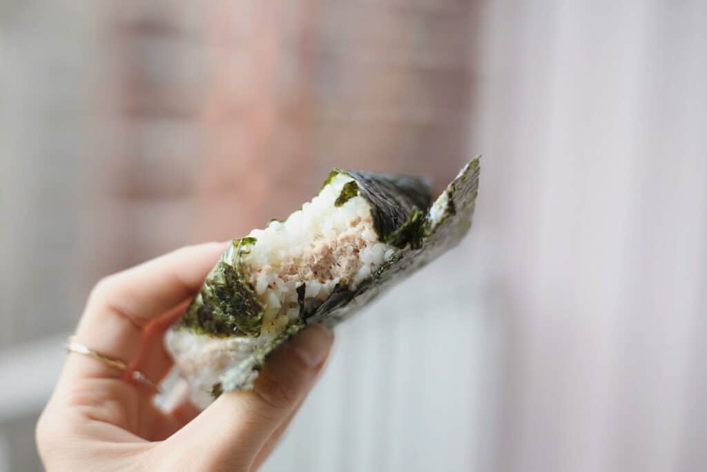 A person eating onigiri in the shape of a triangle 