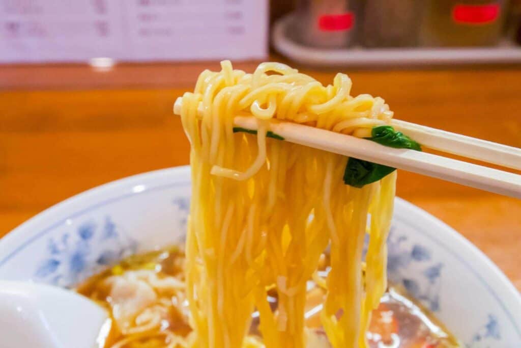 Someone off-screen grabbing noodles with chopsticks