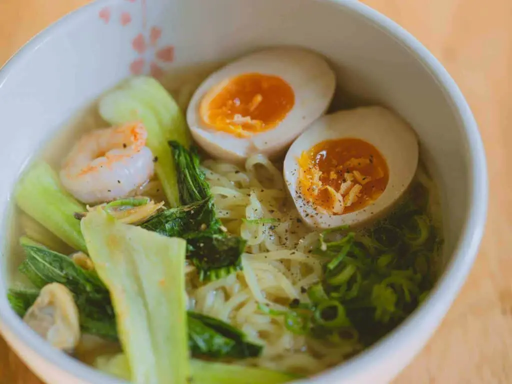 A bowl of ramen with noodles, eggs, and vegetables
