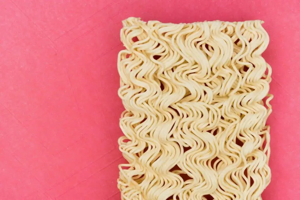 Unprepared instant ramen noodles on a pink surface 
