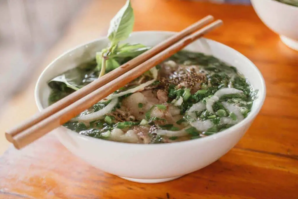 Rice noodles in a broth, served in a white bowl with chopsticks