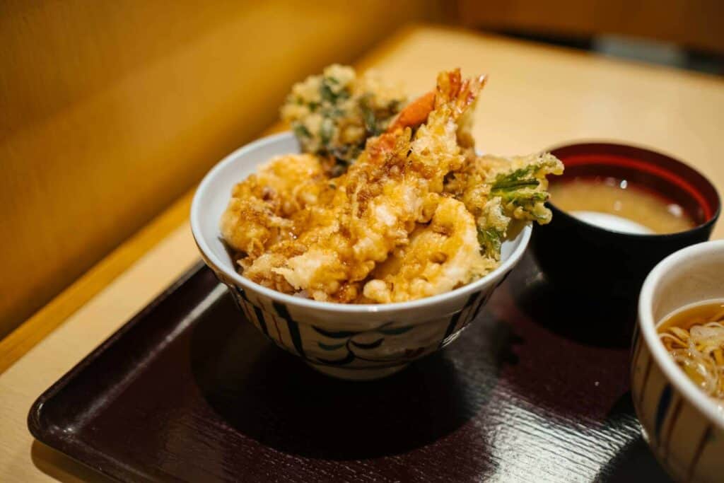 Shrimp tempura, a bowl with soup, and a bowl with noodles next to it 