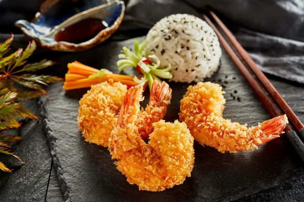 Shrimp tempura and rice on a black board, chopsticks next to tempura 