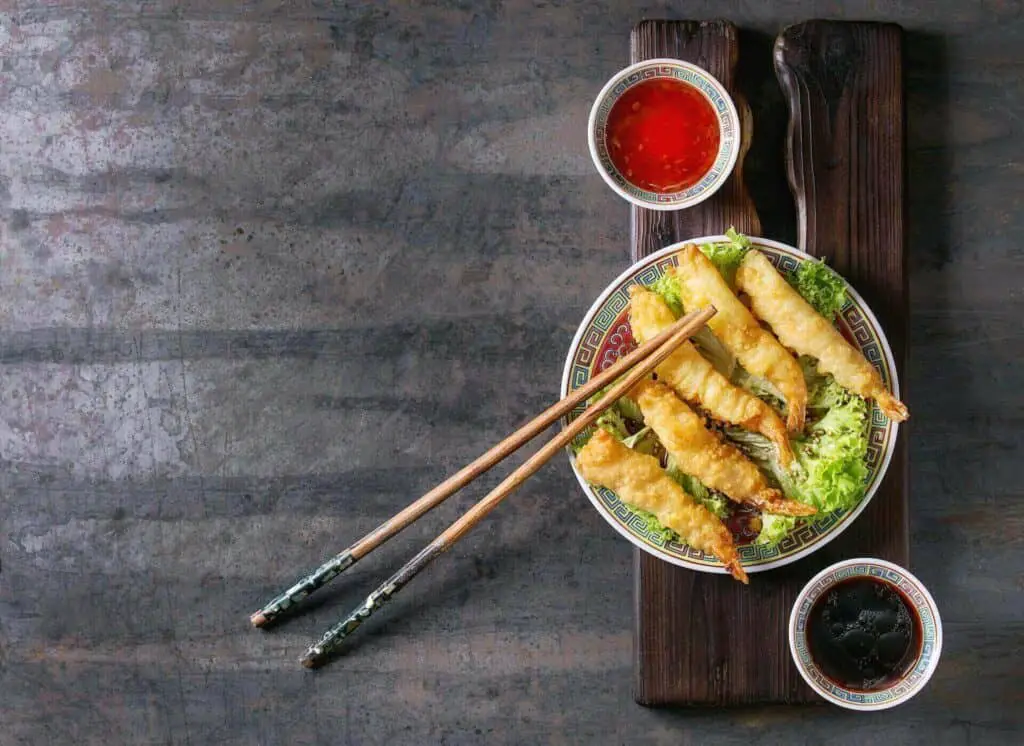 Shrimp tempura on a plate, two bowls with sauce next to it, and chopsticks on the plate