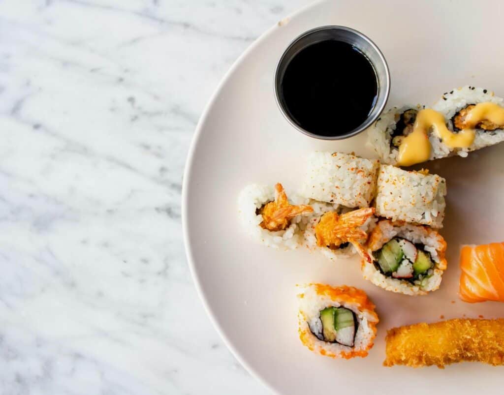 Some shrimp tempura rolls and other kinds of sushi on a plate next to soy sauce