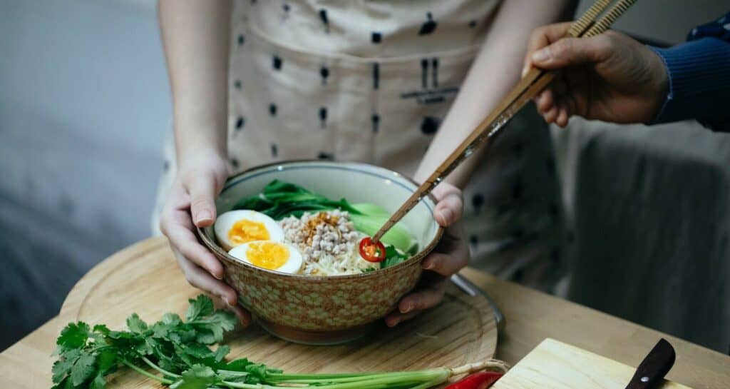 A woman holding a bowl of ramen filled with toppings