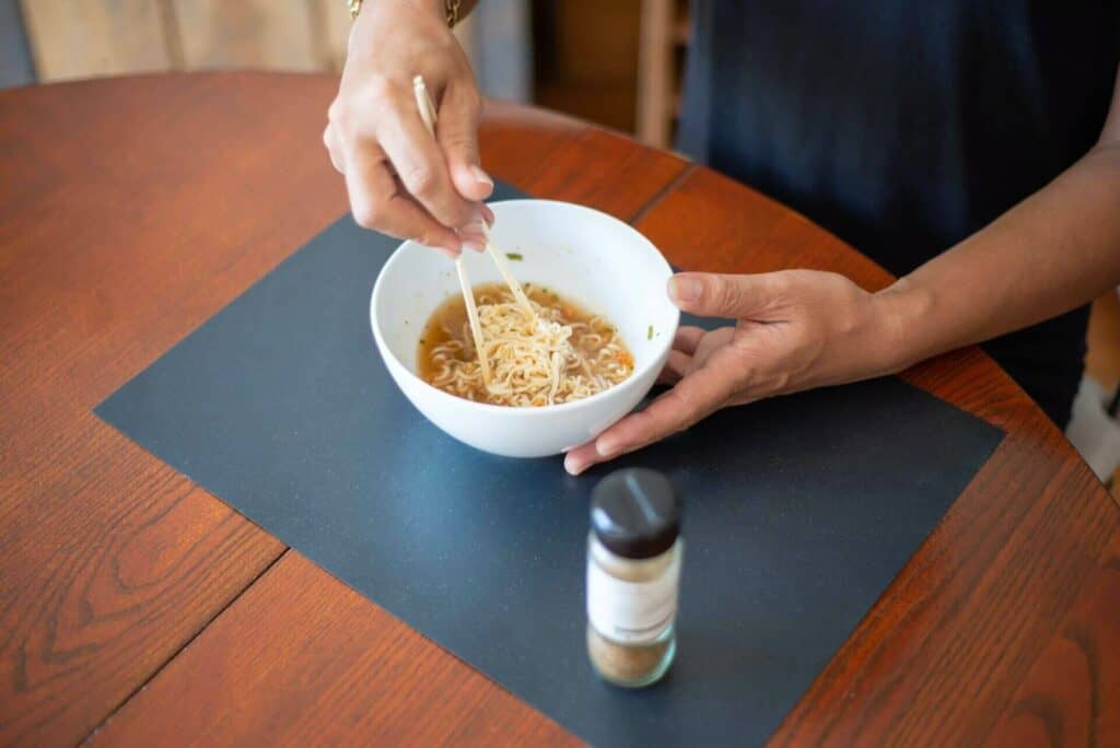 A person stirring instant ramen in a white bowl