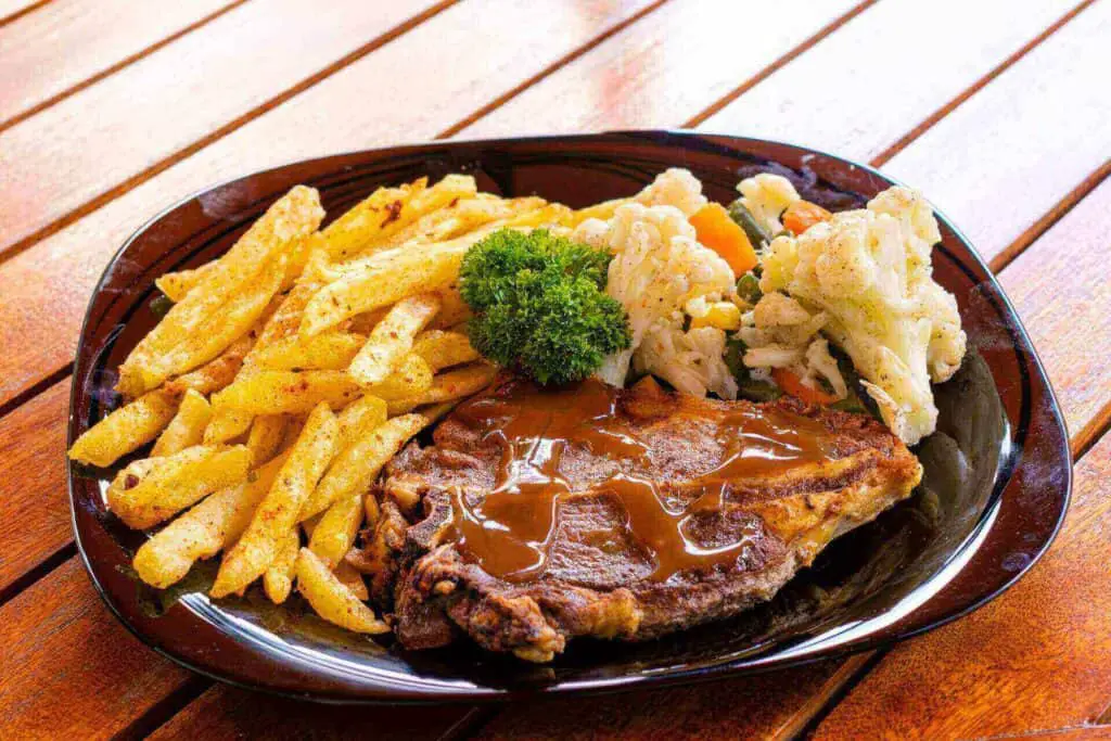 A steak on a plate with fries and sauce